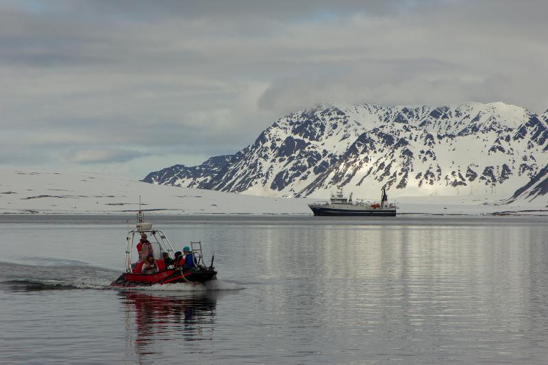 Lettbåten Polarsirkel er på veg inn til Bjørnhamna på Svalbard med folk, forskningsskipet FF Helmer Hanssen ligger ute i fjorden.