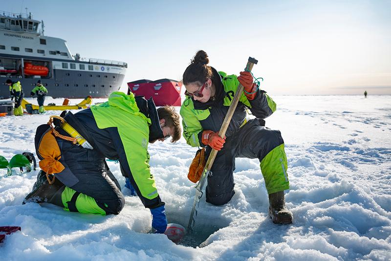 Scientists working on the sea ice. Large research vessel in the background.