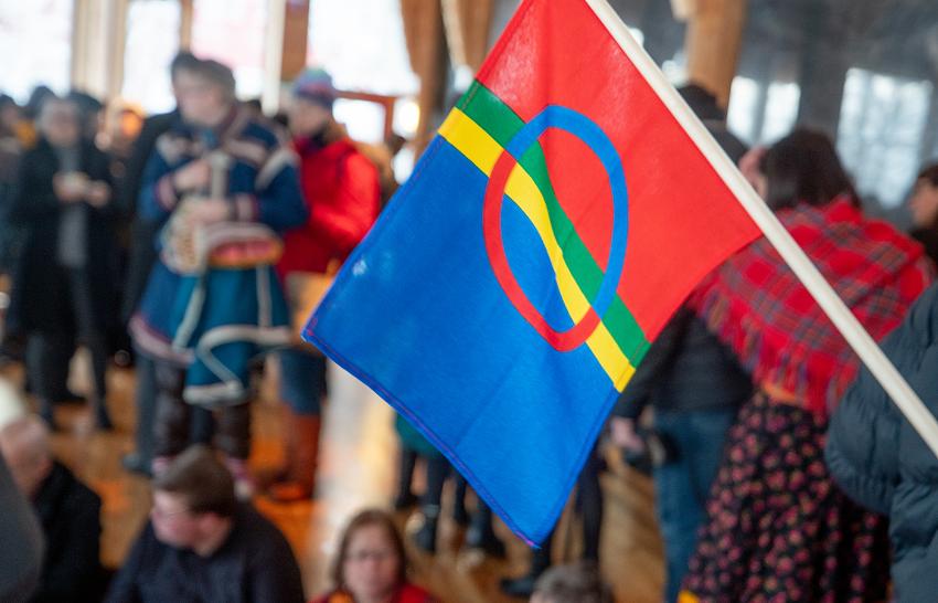 Det samiske flagget og festpyntede personer innendørs.