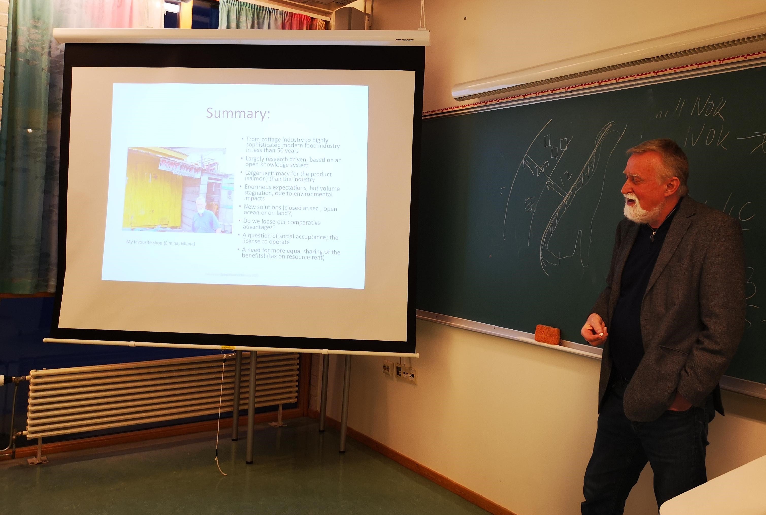 Bildet viser Bjørn Hersoug som står foran en powerpoint og snakker om norsk oppdrettsnæring.