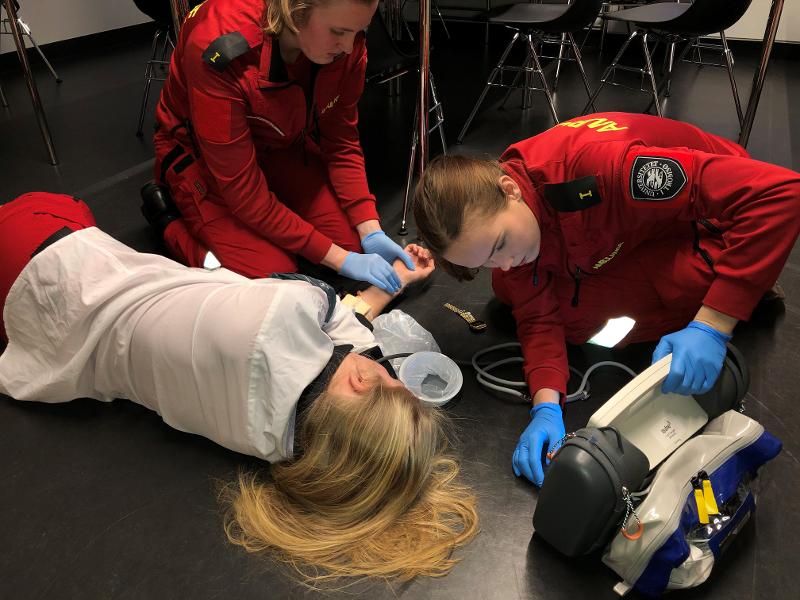 pasient som ligger på gulvet, med student som hjelper til