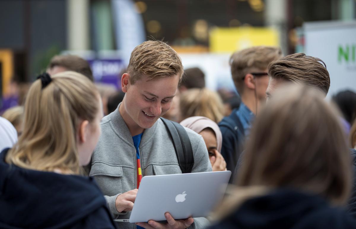 Mann holder en Macbook med flere studenter rundt seg