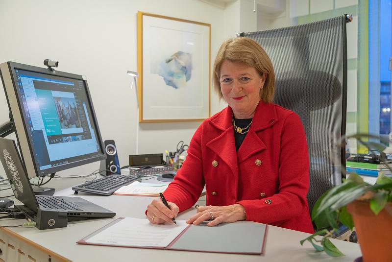 Rektor Anne Husebekk sitter ved et skrivebord og signerer dokumenter