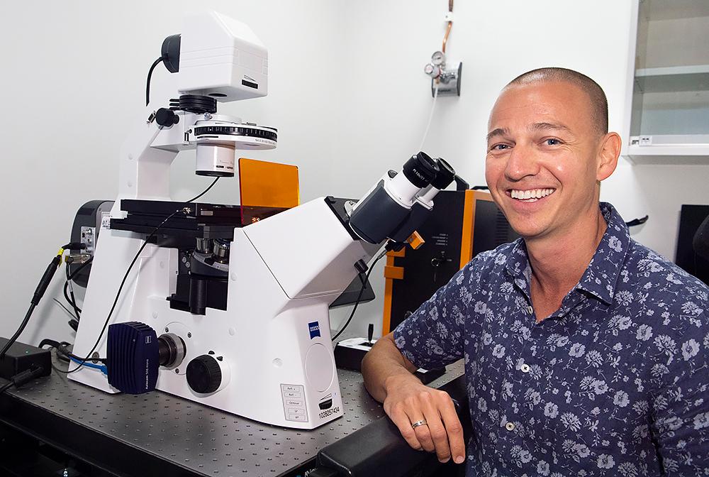 Mann sitter foran et stort mikroskop