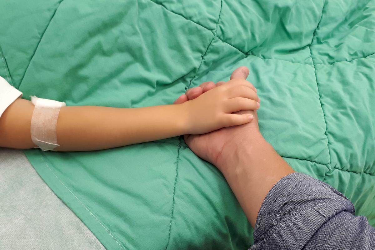 Barnehånd som holder en voksenhånd på et sykehus.