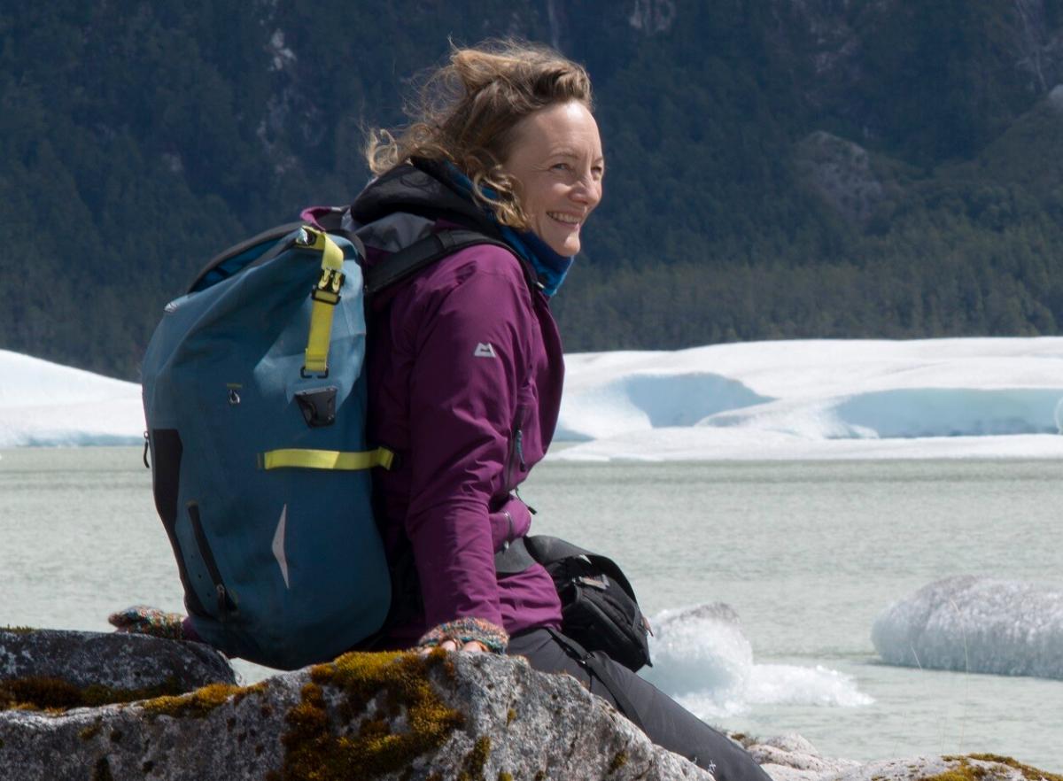 Smilende kvinne med vann, isbre og skog i bakgrunnen