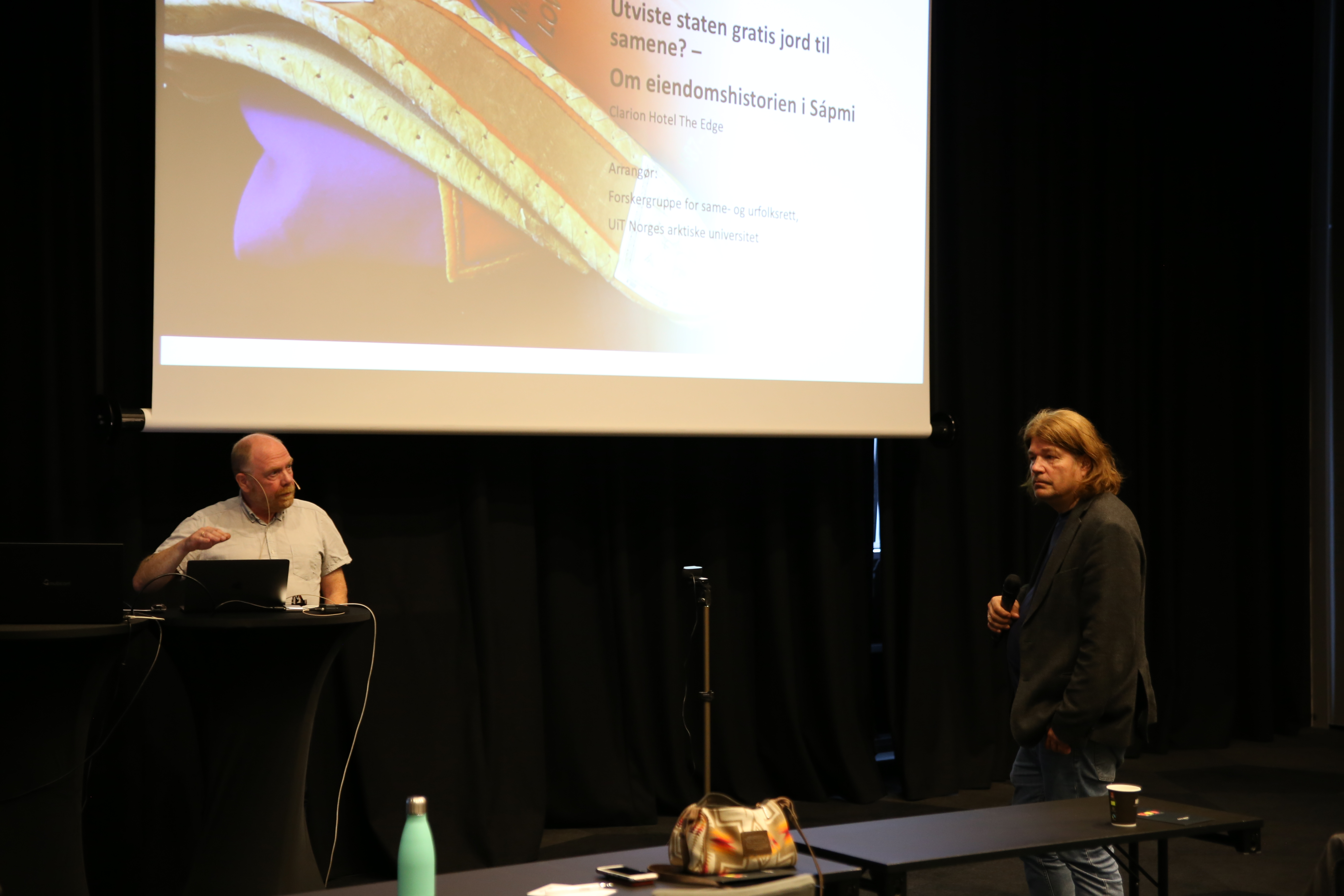 Gunnar Eriksen og Harald Lindback er i samtale. De står begge foran et lerret med en presentasjon på. 