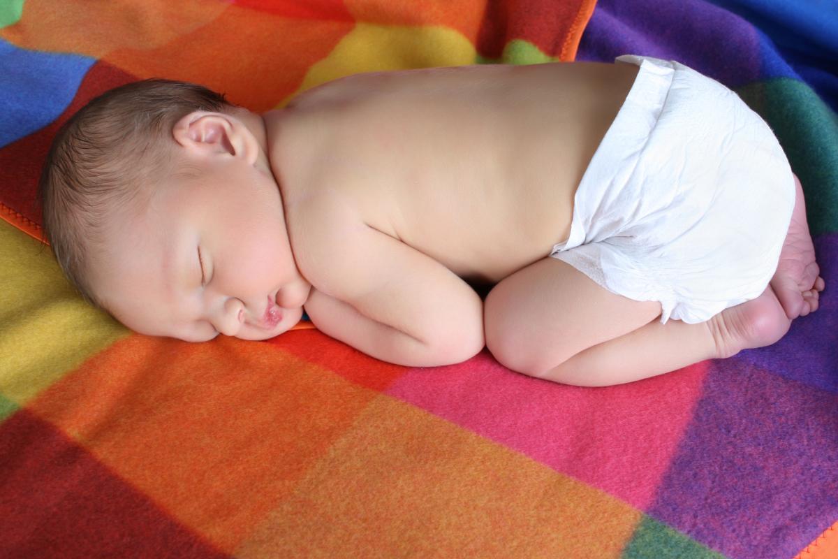 Nyfødt baby ligger på magen på et fargerikt teppe.