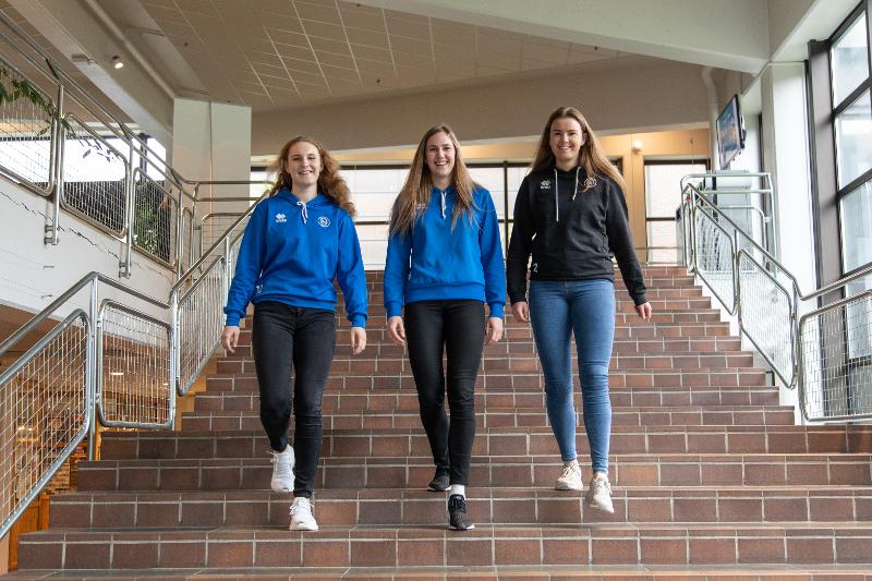 Tre unge kvinner går ned trapp på UiT, smilende i kamera