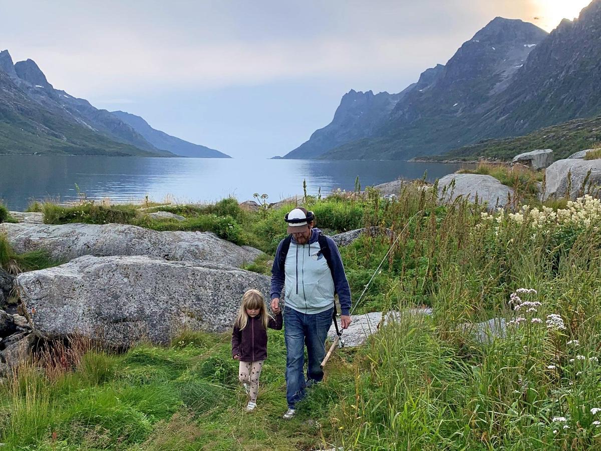pappa som holder datter i hånda ute i naturen med en fiskestang i handa