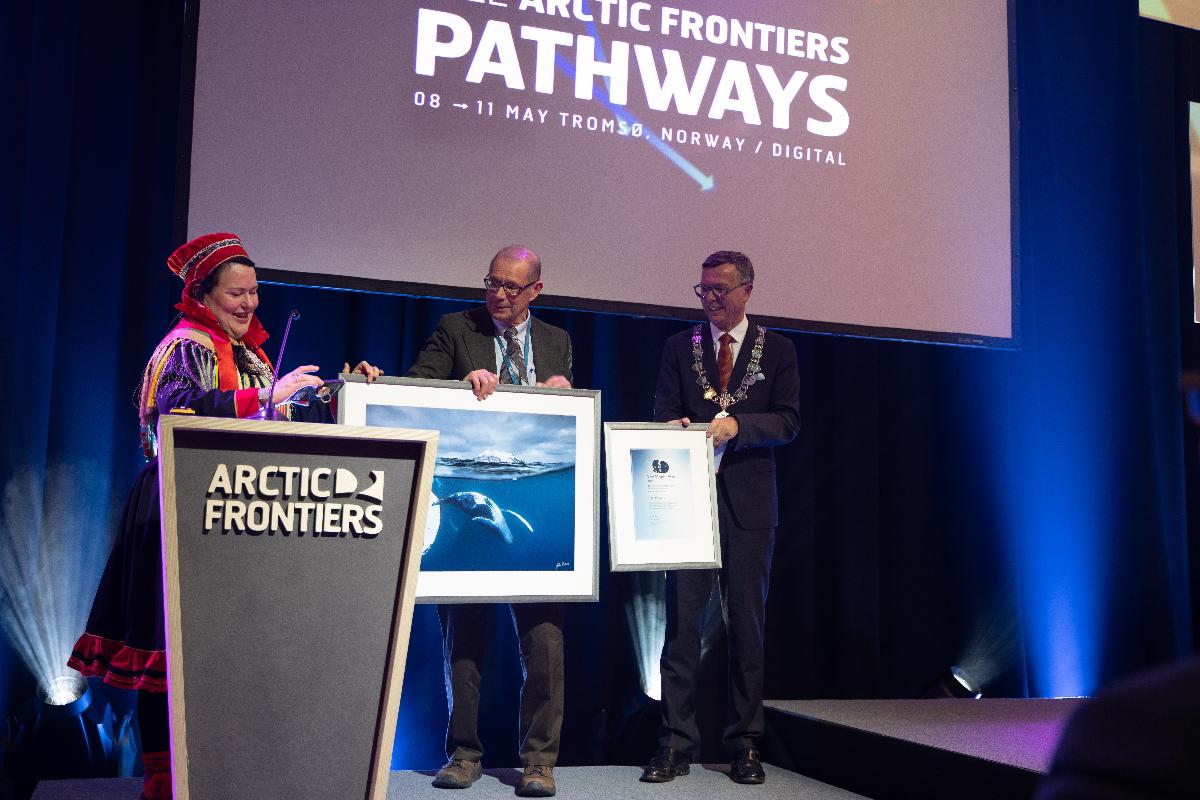 Professor John E. Walsh mottok Mohnprisen 2022 av sametingspresident Silje Karine Muotka under Arctic Frontiers-konferansen mandag ettermiddag. Til høyre står rektor ved UiT, Dag Rune Olsen. 