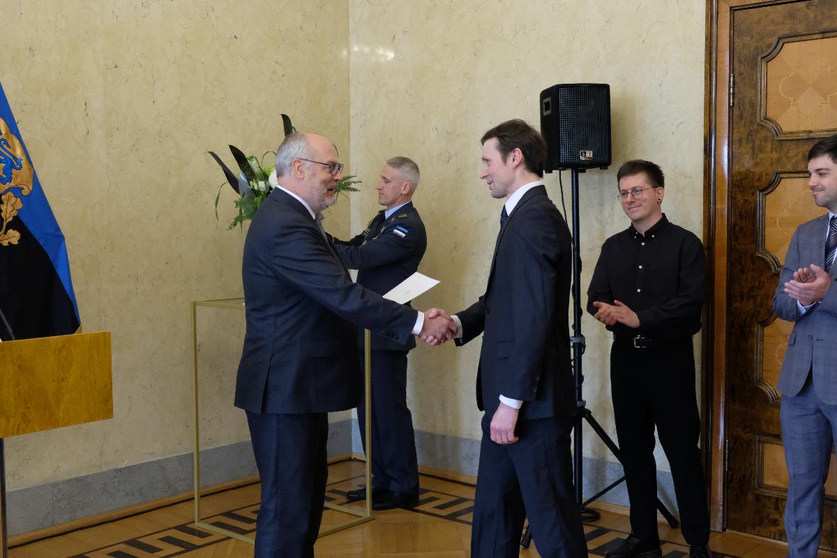 Alexander Lott mottar prisen for unge forskere fra den estiske presidenten Alar Keris. To personer står i bakgrunnen og klapper, en person tar tilsynelatende et selfie. 