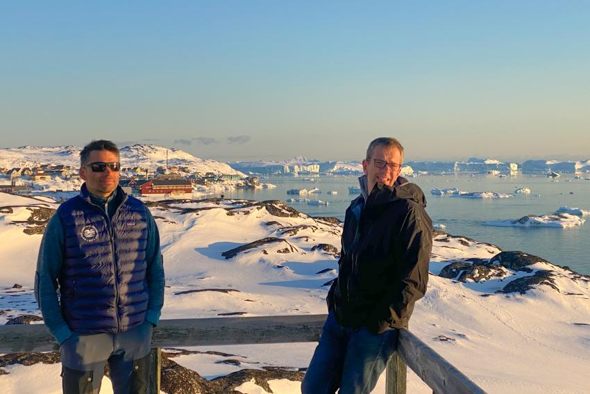 To menn står på ein terasse i Illusat, byen, havet og isen i bakgrunnen.