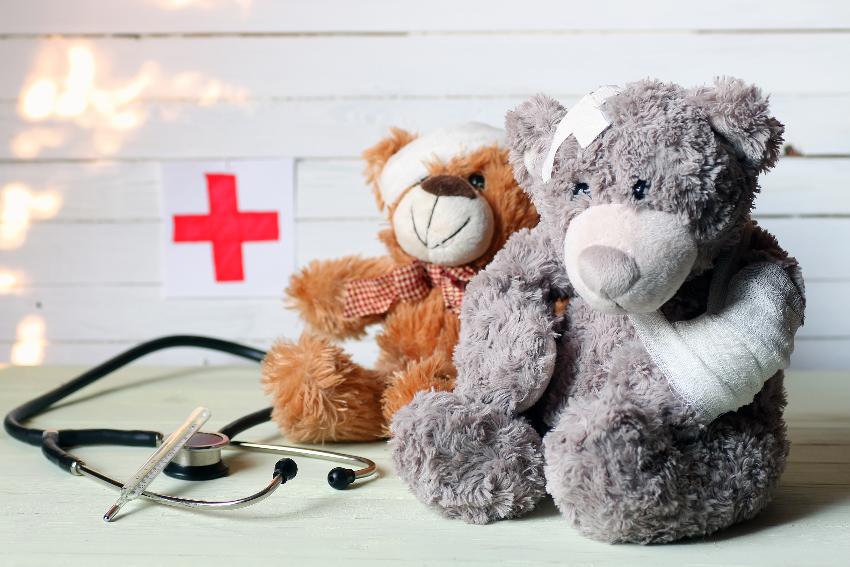 To teddybjørner som er bandasjert. Til høyre ligger et stetoskop, over stetoskopet er et rødt kors.