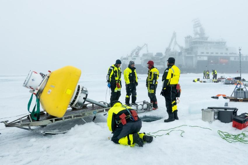 Forskingsbøye på isen på Nordpolen. Mykje utstyr og forskarar. I bakgrunnen RV Kronprins Haakon.