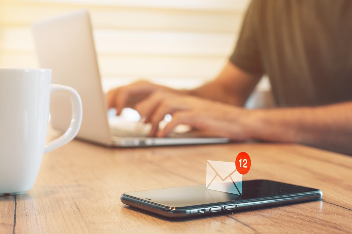 Mobile phone on a table and hands writing on a laptop