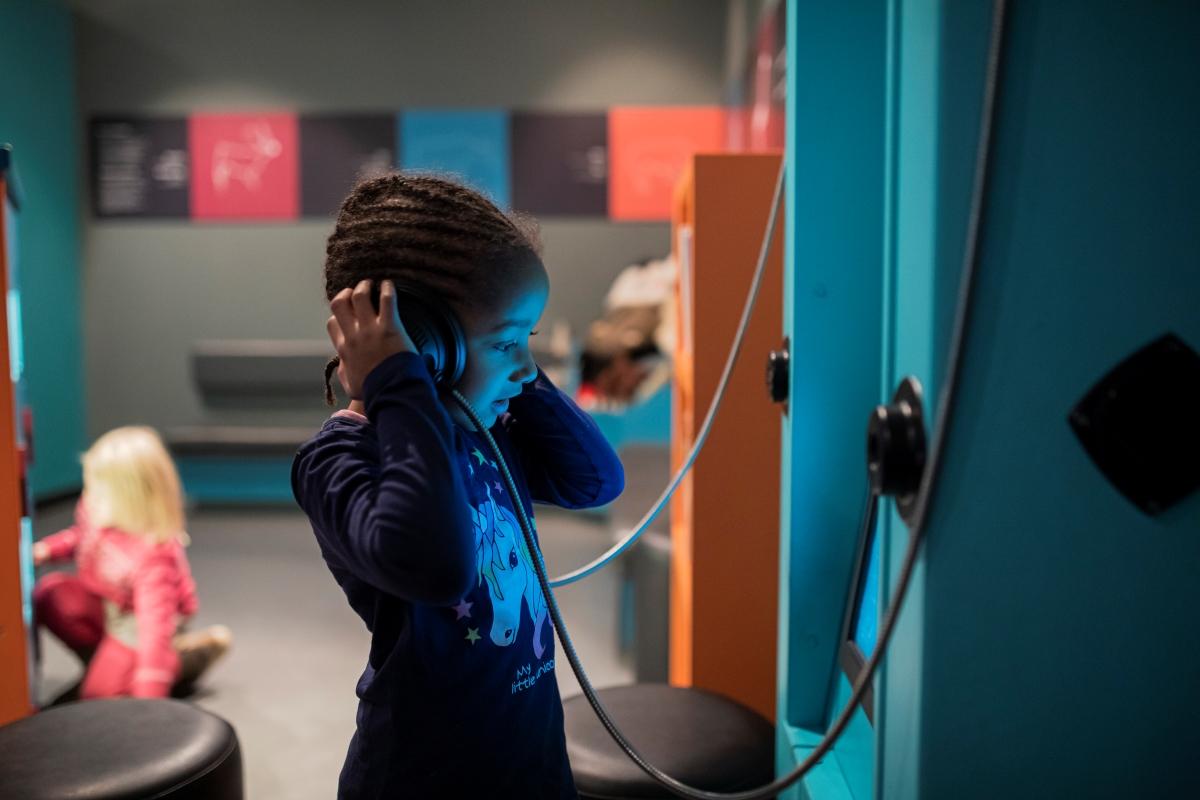 Ei jente lyttar på hodetelefonar på eit museum