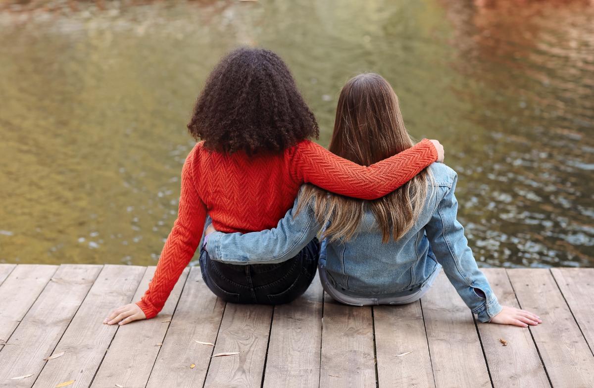 To jenter som sitter på en brygge med ryggen til.