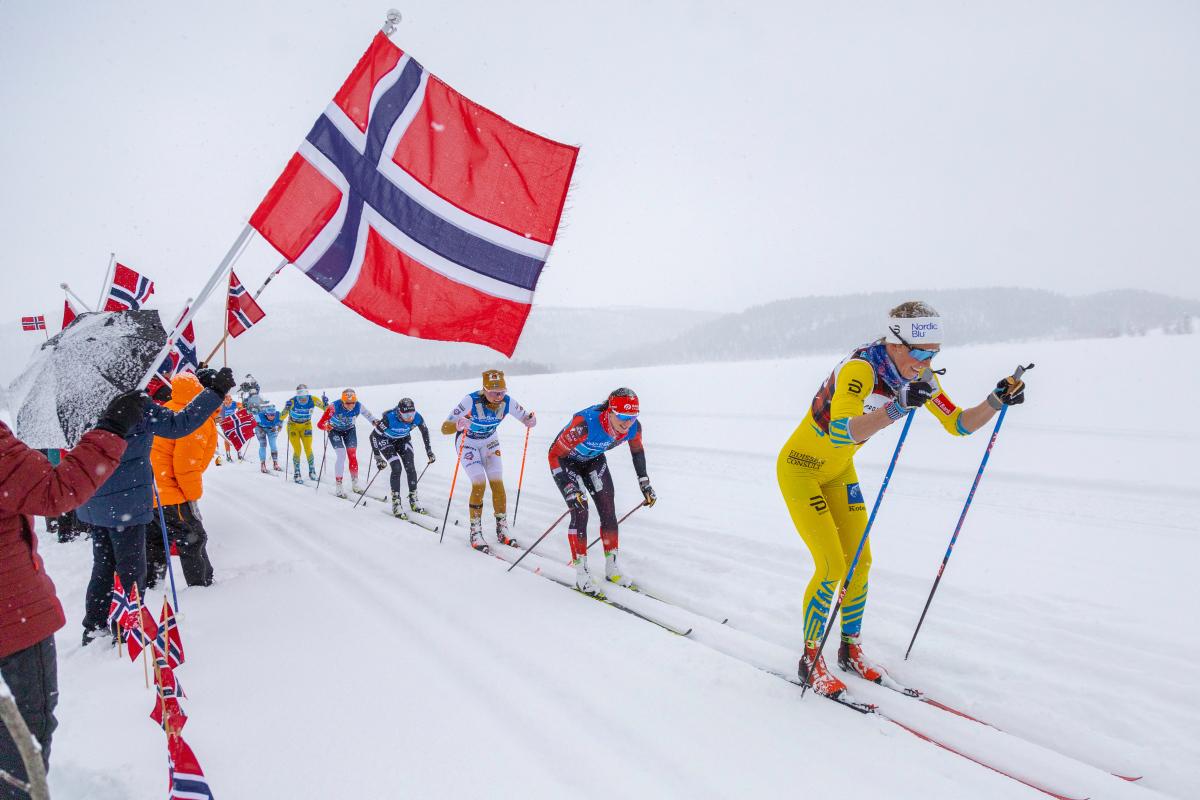 Skiløpere i skisporet passerer publikum som vaier med et norsk flagg.