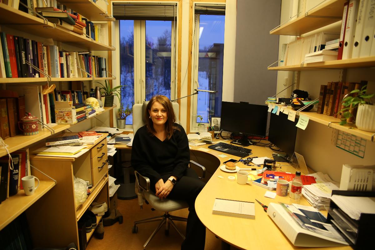 Et bilde av Lisa Mattea Elvevoll som sitter på en stol inne på sitt kontor, det er veldig rotete på kontoret...