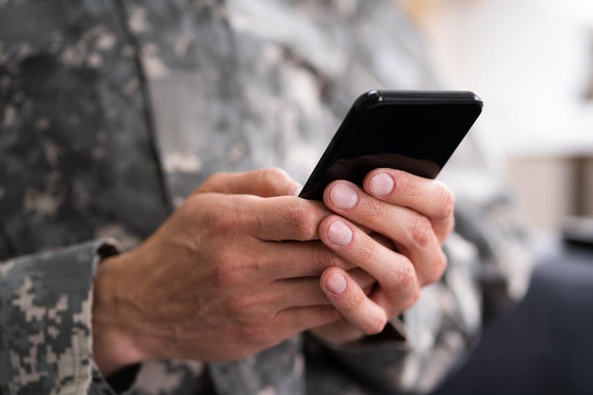 Bilde av en soldat som holder en smartphone i hendende sine. 