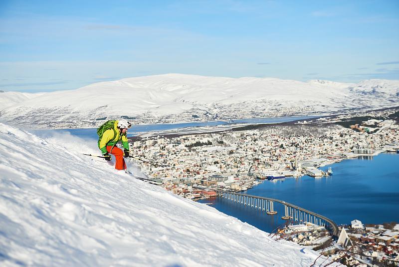 En mann kjører på ski ned fra et fjell, Tromsøya er i bakgrunnen. 