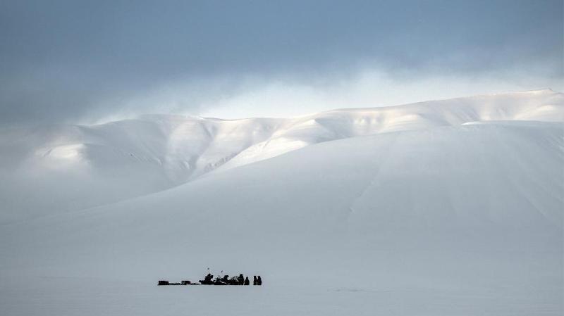 et islandskap, en gruppe mennesker litt unna, store hvite fjell og himmelen i bakgrunnen