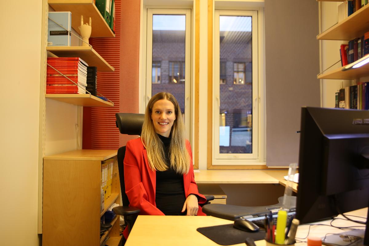 Kristine alteren sitter på kontoret sitt og smiler til kameraet. 