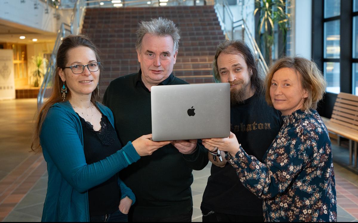 To kvinner og to menn holder en Apple-laptop mot kamera.
