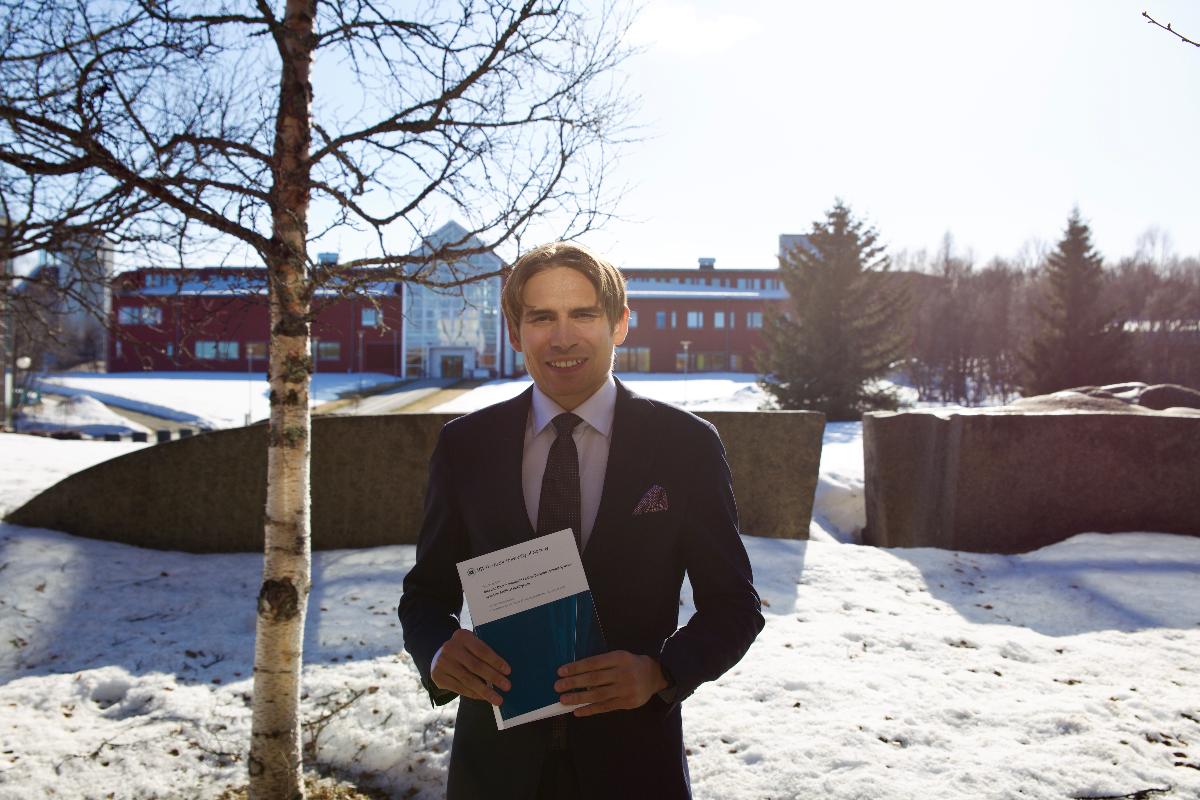Mathias står foran administrasjonsbygget med sin avhandling i sollyset.