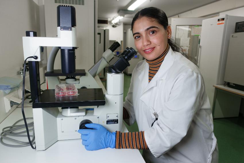 En kvinne i labfrakk poserer sittende ved et mikroskop