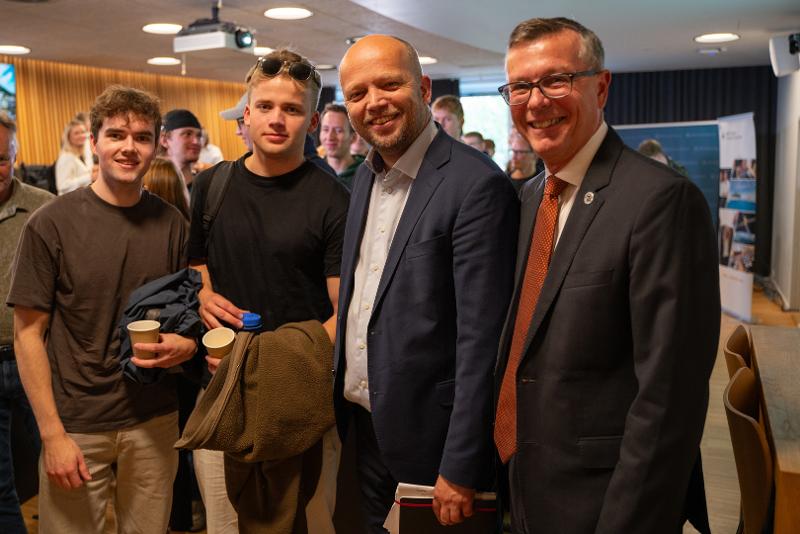 Fire menn i auditorium. To unge studenter, samt minister og universitetsrektor. 