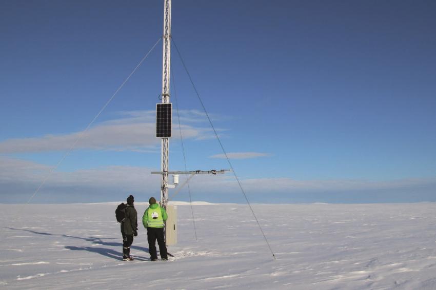 To personer står ved en høy antenne på en isdekket tundra.