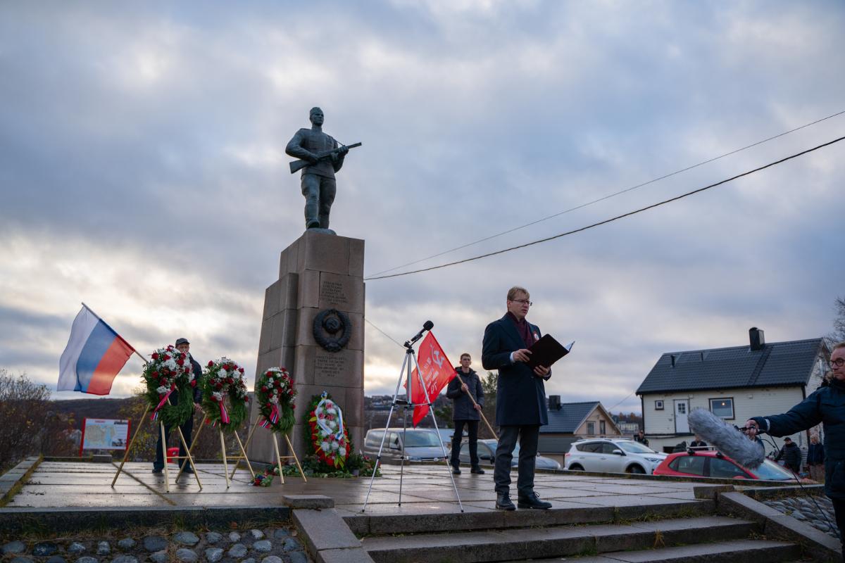 Person standing in front of a monument with several others holding flags.