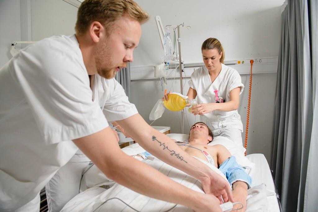 Two persons in hospital garb helping a patient in a hospital bed.