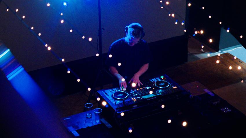 mannlig DJ snurrer plater, sett ovenfra gjennom stemningsfulle lyslenker