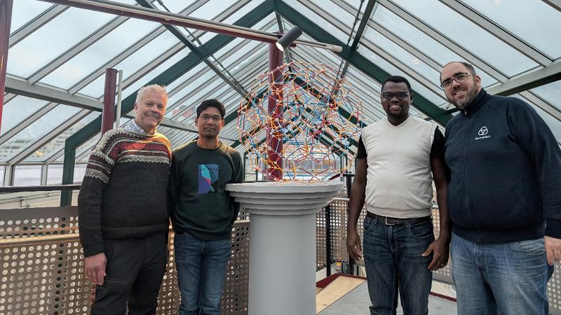 four men standing around a technological figure