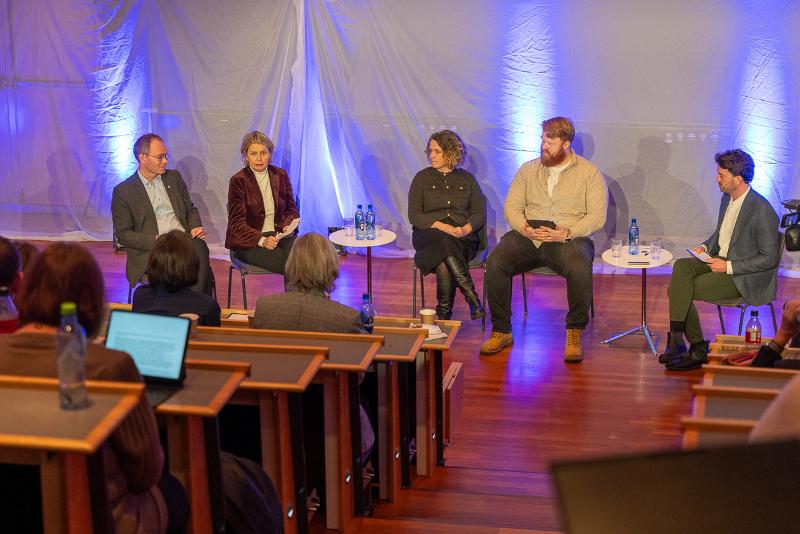 Fem menneske i ein paneldebatt fremst i eit auditorium.