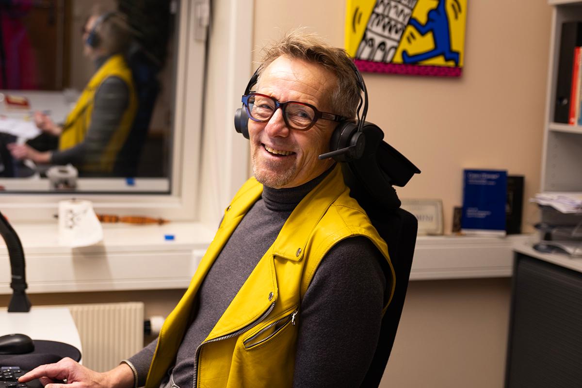 En smilende mann på et kontor. Han har på headset med mikrofon.