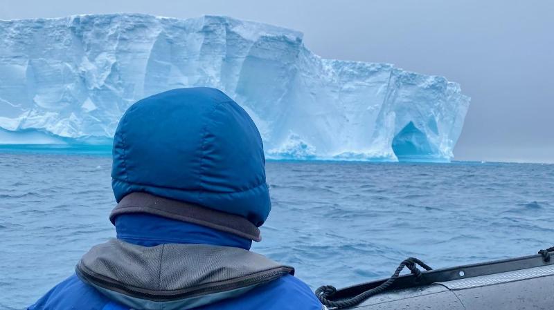 a person in a rib boat looking at an enormous ice berg