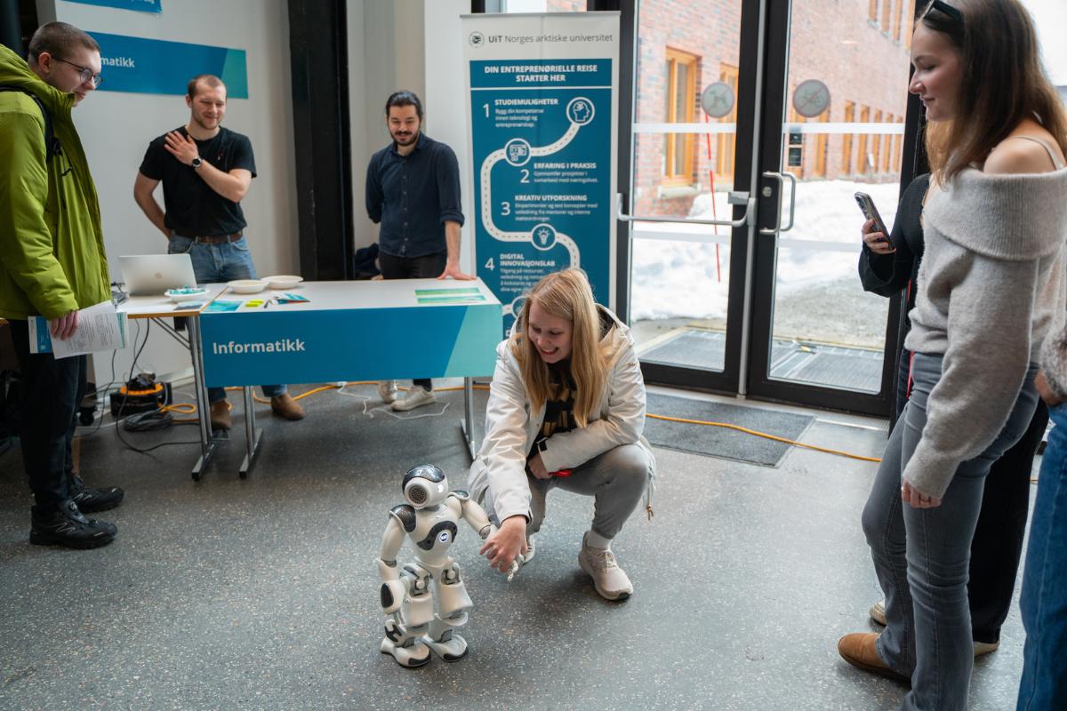 jente som sitter på huk og hilser på en liten robot på gulvet