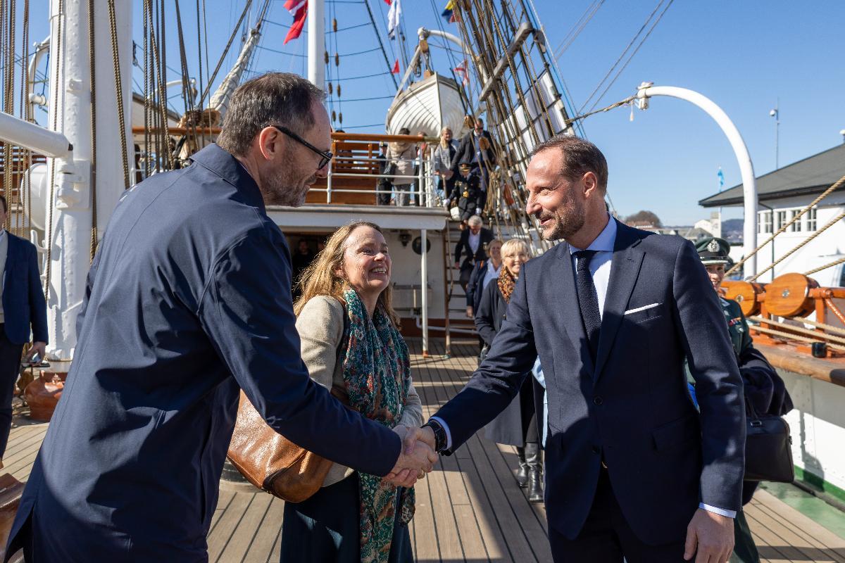 To personer håndhilser om bord på et seilbåtdekk.