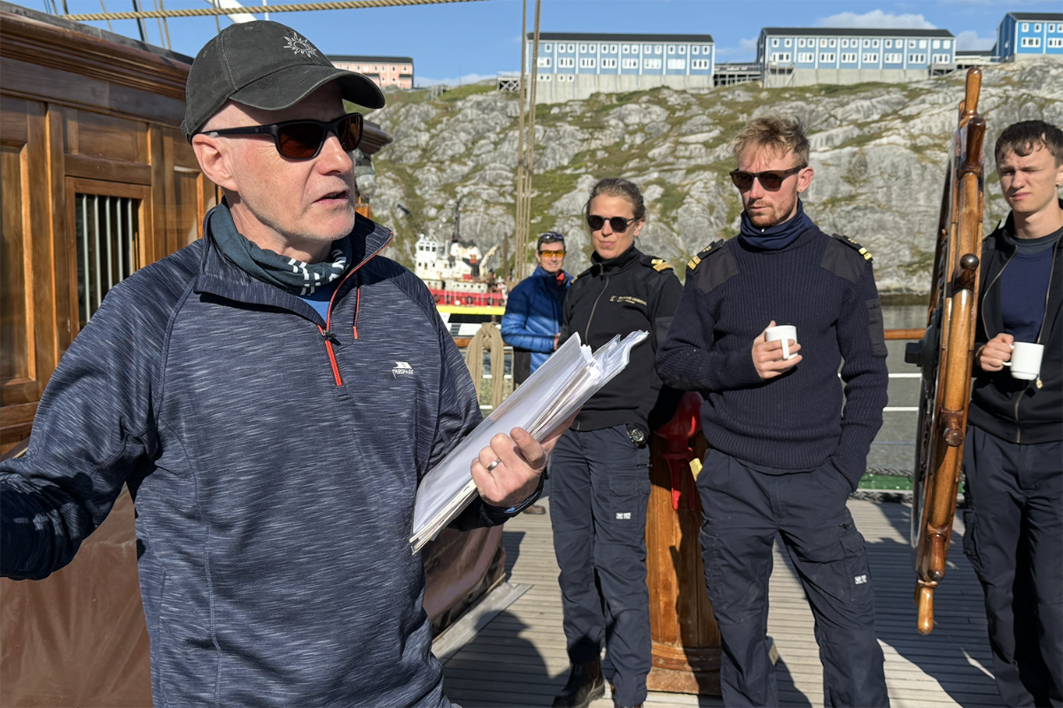 En mann står og snakker med andre personer om bord på et skip