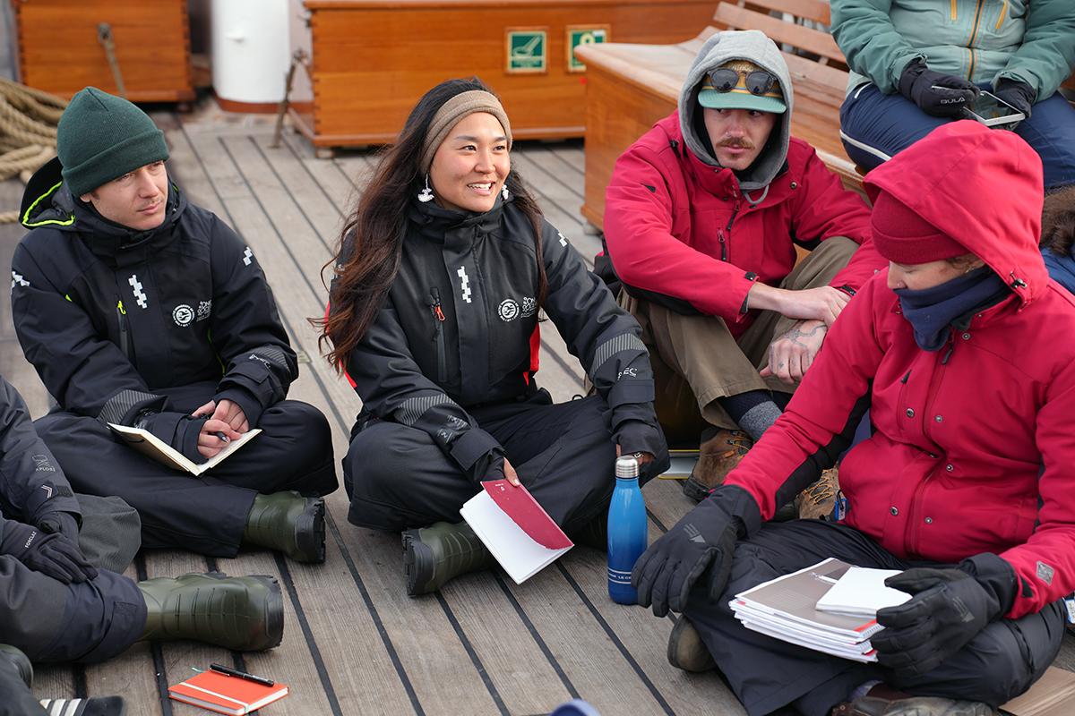 Flere personer sitter ved siden av hverandre og snakker på dekket av et skip