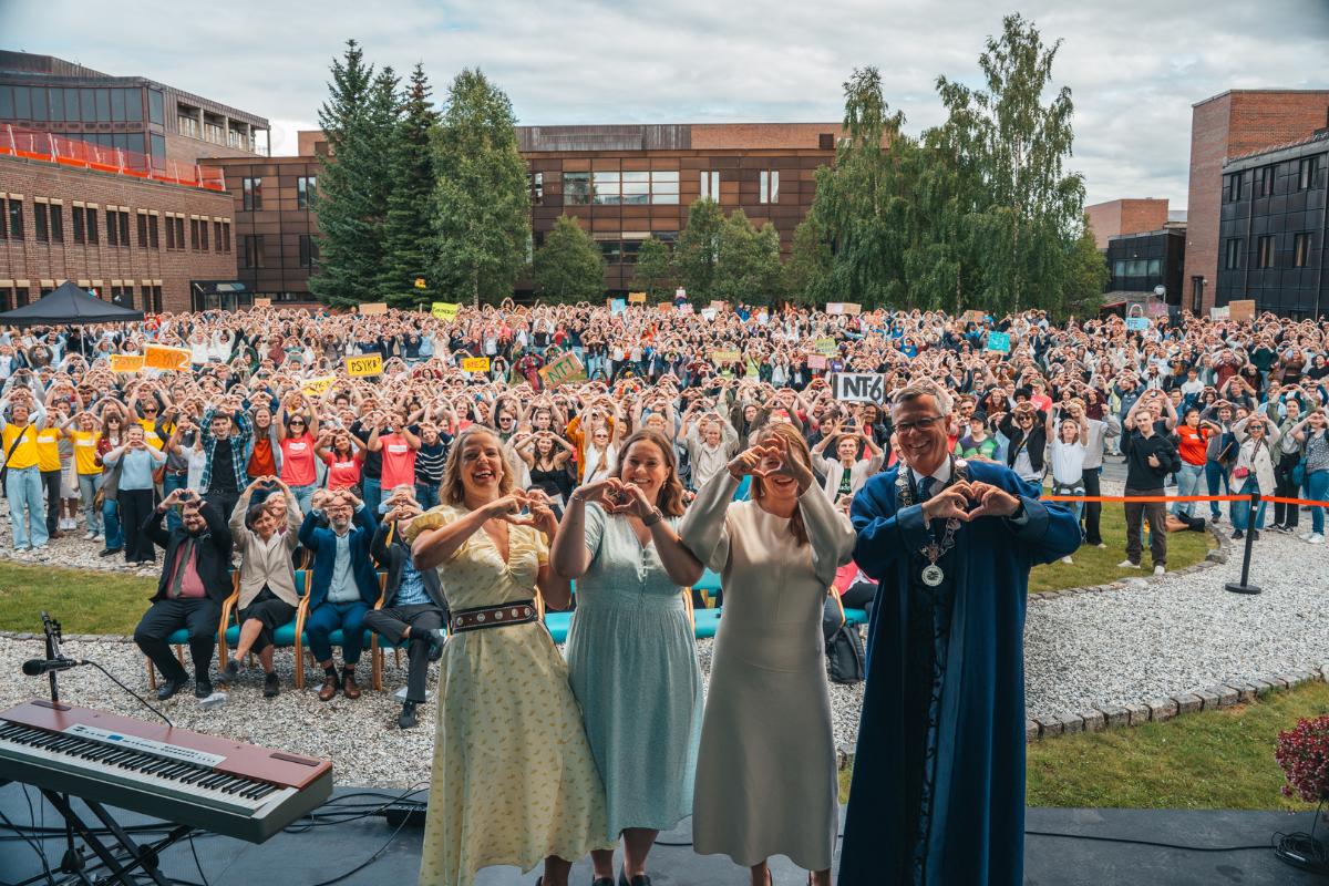 Rektoratet ved UiT, samt næringsminister viser hjertesymbol med hendene sammen med tusenvis av studenter og ansatte på universitetsområde.