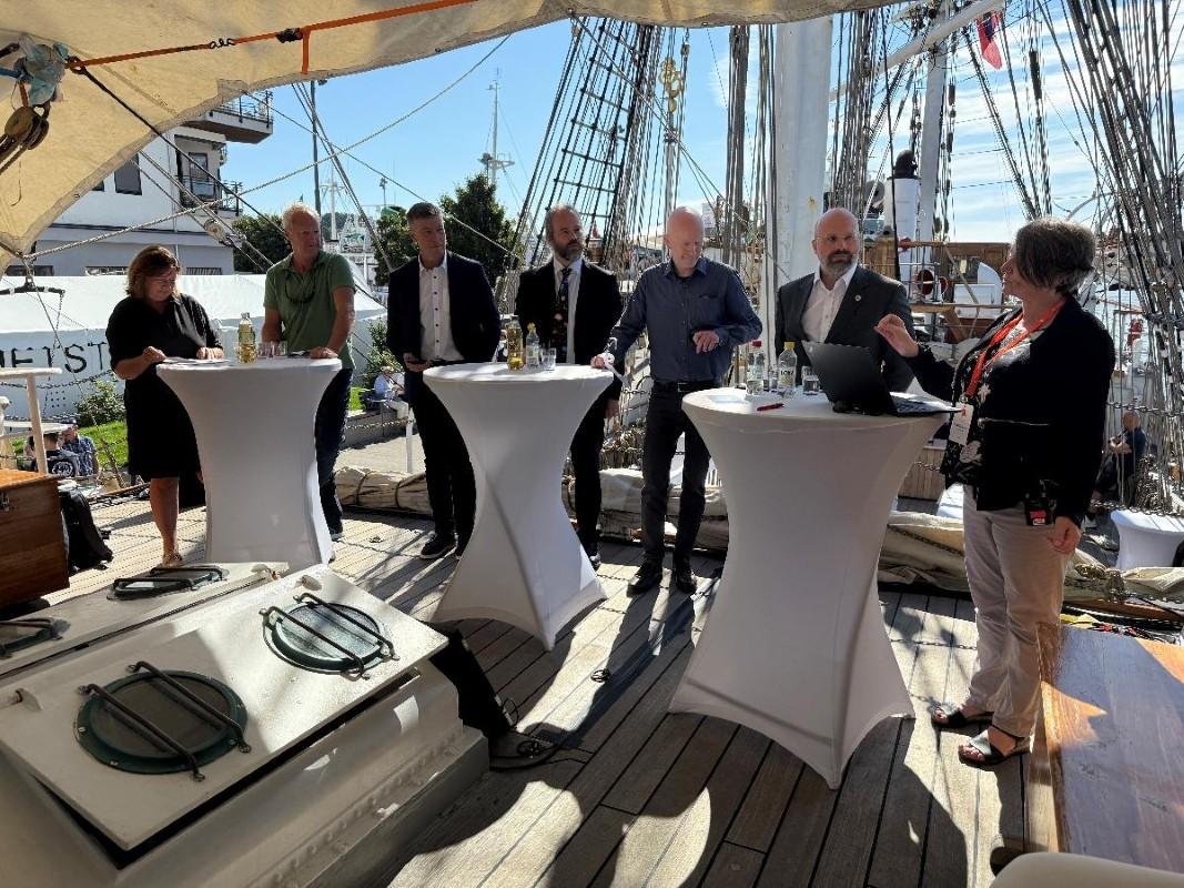 Bilde av flere folk i en paneldebatt på et skip