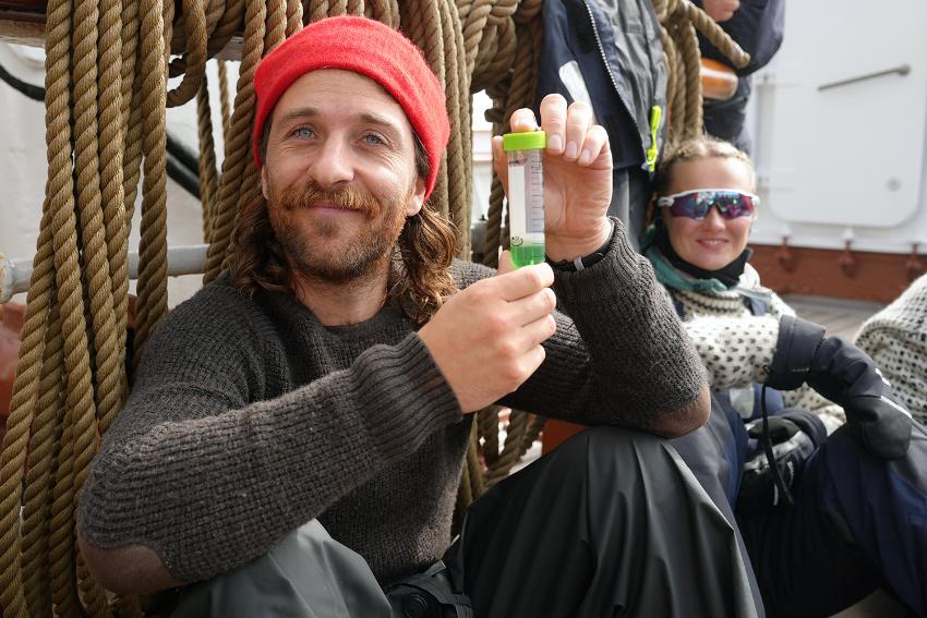 Person sitter med et reagensglass og smiler