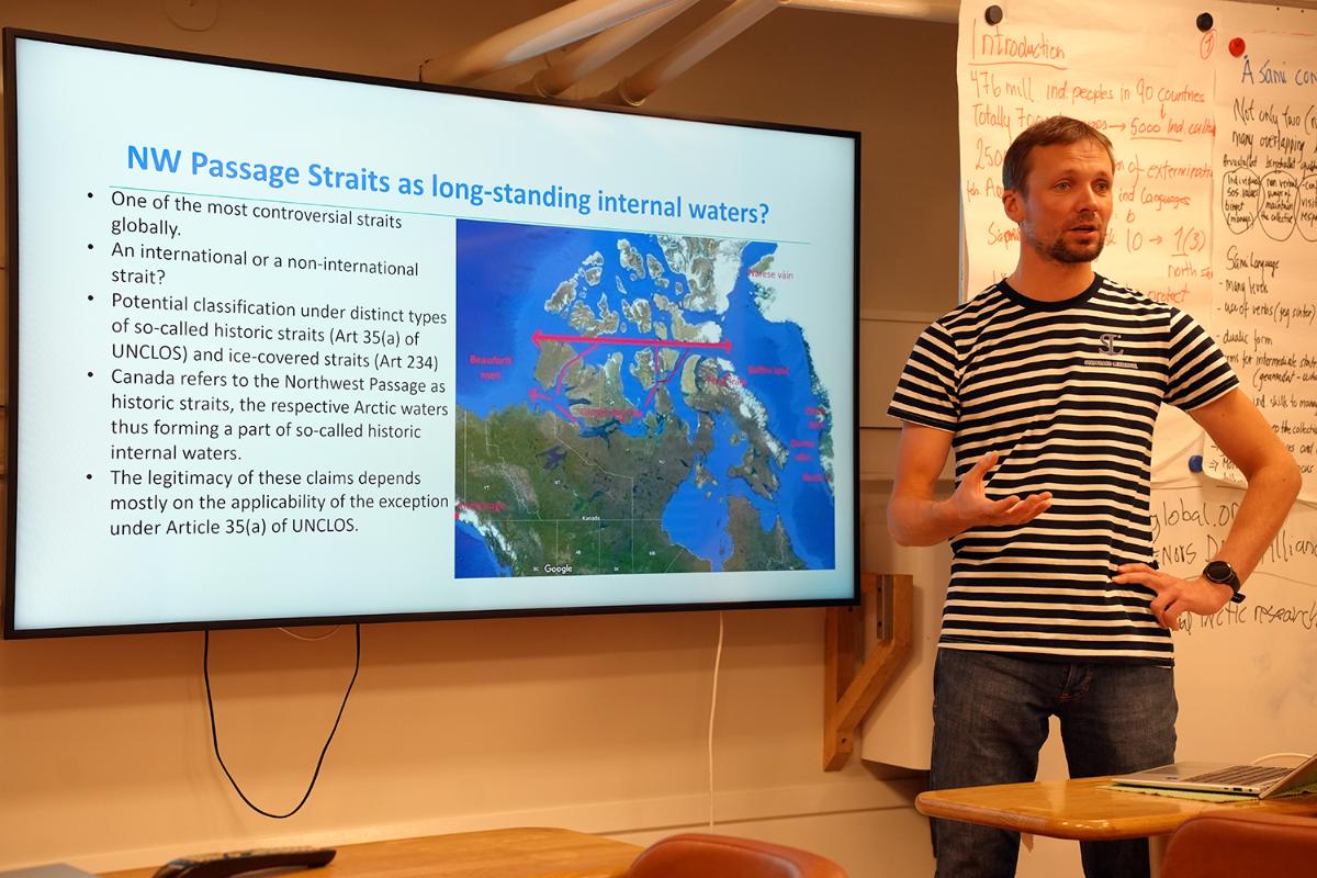 A person standing in front of a power point presentation, talking. 