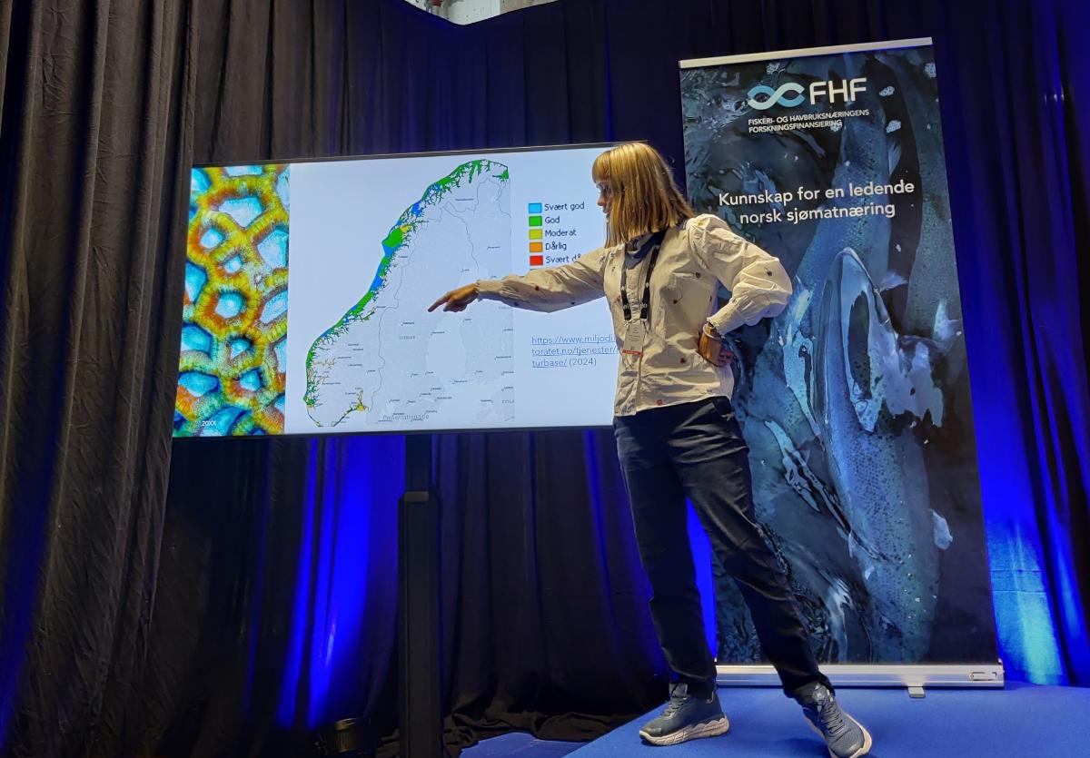 Lena Schøning står på scene og presenterer til et publikum. 