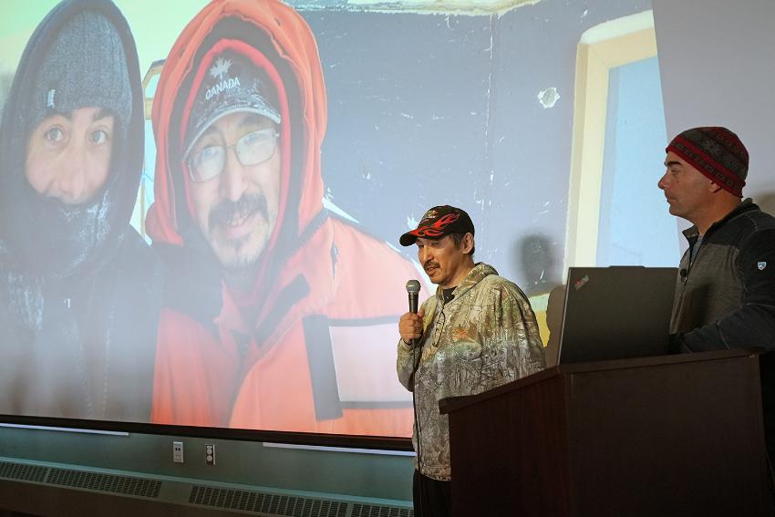 To menn snakker foran et stort bilde